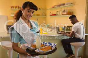 Waitress holding breakfast while man working on laptop