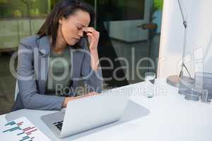 Tensed businesswoman sitting with laptop at desk