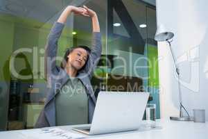 Tired businesswoman stretching her arms up at desk