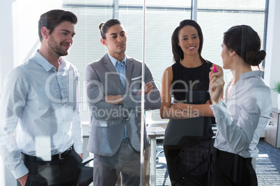 Female executive with his colleagues discussing over glass board