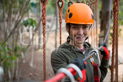 Young smiling woman holding zip line cable in the forest during daytime