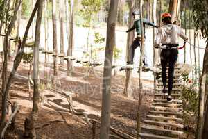 Couple walking on wooden obstacle bridge in the forest