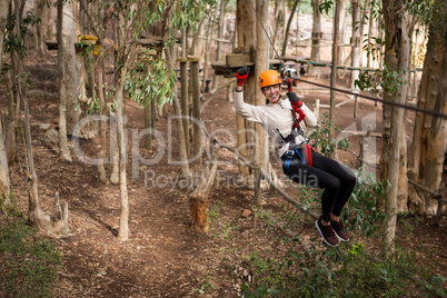Happy woman wearing safety helmet riding on zip line in the forest