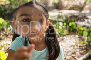 Little girl holding and looking through magnifying glass in the forest