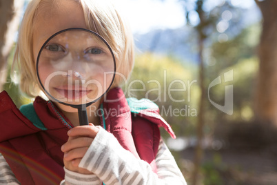 Little girl looking through magnifying glass in the forest