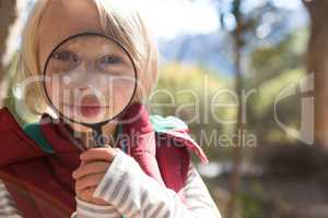 Little girl looking through magnifying glass in the forest