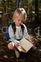 Little girl with backpack sitting on ground writing in notebook