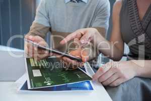 Mid section of business executives discussing over digital tablet