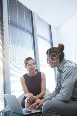 Colleagues interacting with each other while using laptop