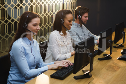 Business executives with headsets using computers at desk