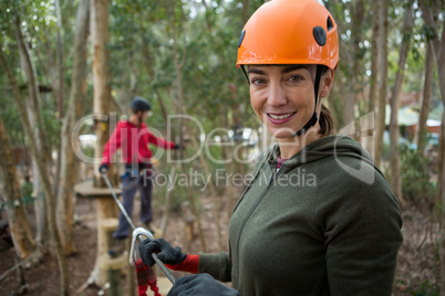 Smiling young woman holding zip line cable and standing in the forest during daytime
