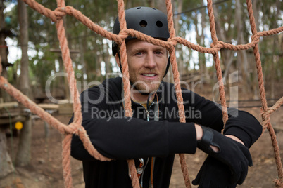 Man wearing safety helmet leaning on rope fence in the forest