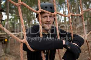 Man wearing safety helmet leaning on rope fence in the forest