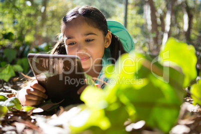 Little girl with backpack lying on ground using her tablet on a sunny day