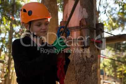 Little girl wearing helmet fixing harness on zip line