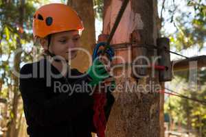 Little girl wearing helmet fixing harness on zip line