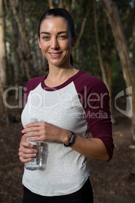 Woman standing in forest holding water bottle