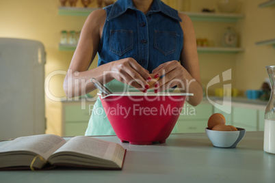 Young woman breaking an egg in to mixture bowl