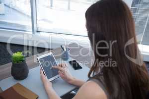Rear view of female executive using digital tablet at desk