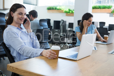 Female executive talking on phone while holding coffee mug Female executive talking on phone while holding coffee mug