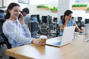 Female executive talking on phone while holding coffee mug