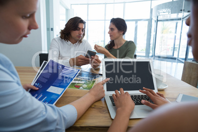 Group of colleague discussing over mobile phone and laptop at desk