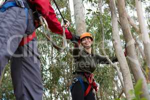 Man helping woman to cross zip line in the forest