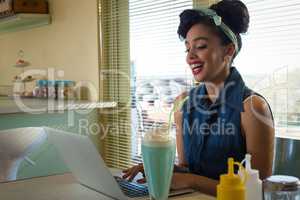 Smiling young woman using laptop while having milkshake