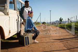 Couple sitting on suitcase at countryside