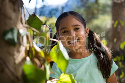 Happy little girl holding magnifying glass in the forest