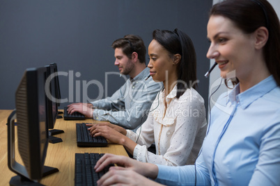 Business executives with headsets using computers at desk