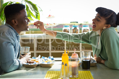 Couple sitting together in restaurant while woman feeding food