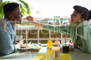 Couple sitting together in restaurant while woman feeding food