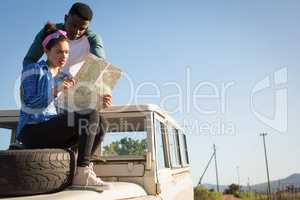 Couple looking at map while sitting on car bonnet