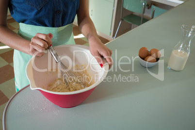 Young woman whisking mixture into bowl in the kitchen