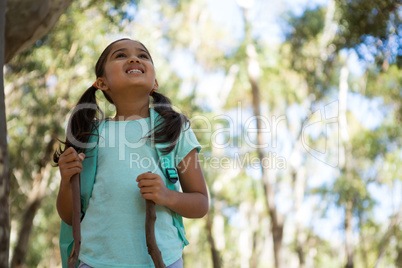 Little girl with backpack holding walking sticks looking up in the sky