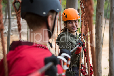 Smiling young woman looking at man while crossing zip line