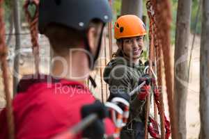 Smiling young woman looking at man while crossing zip line