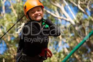 Little girl wearing helmet standing near zip line in the forest