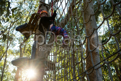 Little girl wearing helmet climbing on rope fence