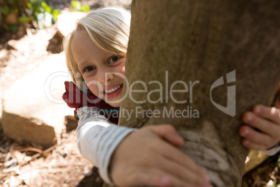 Happy little girl hugging tree trunk on a sunny day in the forest