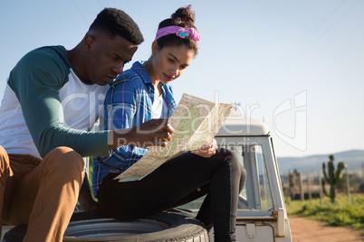Couple looking at map while sitting on car bonnet