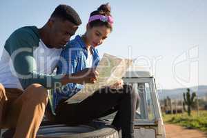 Couple looking at map while sitting on car bonnet