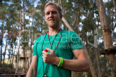 Trainer holding whistle in his hands on a sunny day in the forest