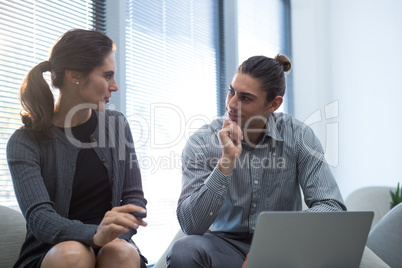 Colleagues interacting with each other while using laptop