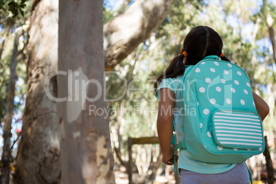 Little girl standing with backpack looking up in the sky on a sunny day