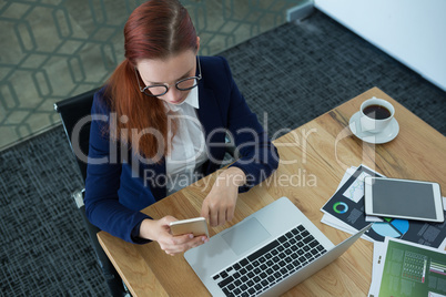 High angle view of female executive using mobile phone at desk