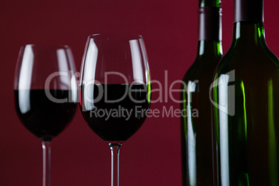 Wine glasses and bottles against red background