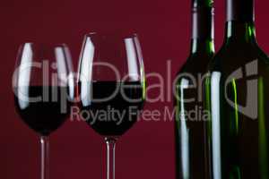 Wine glasses and bottles against red background