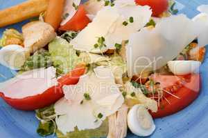 Fresh salad of chicken with vegetables and cheese, on a blue background